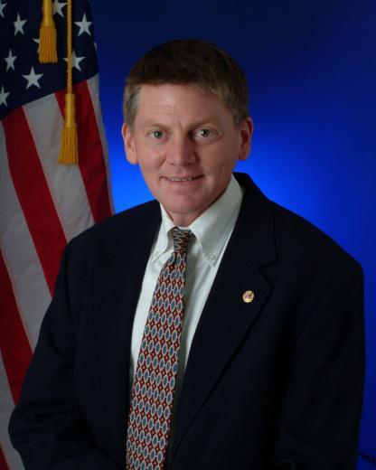 Headshot of Director Kevin Klein sitting in front of an American Flag